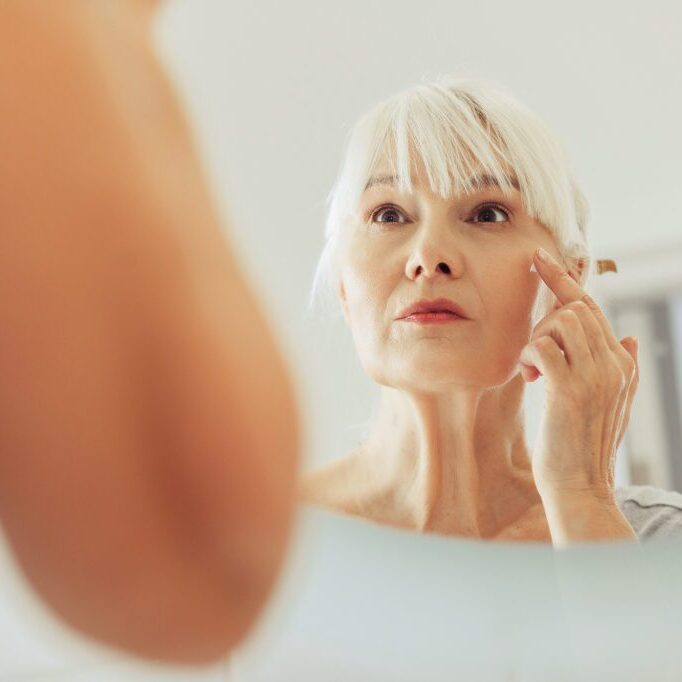 Caring about skin. Reflection of a nice aged woman while putting on cream