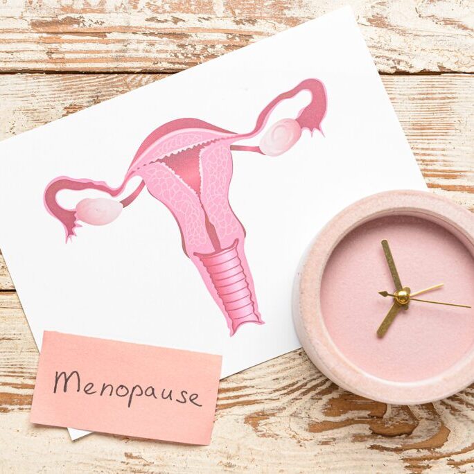 Papers with word MENOPAUSE, uterus and alarm clock on light wooden background